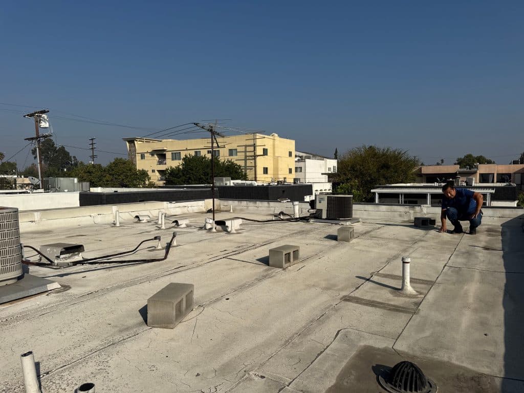 Roofer inspecting a commercial flat roof with rooftop equipment