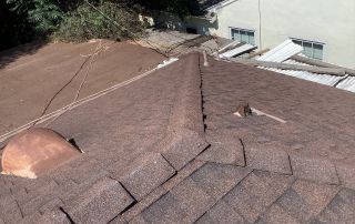 Brown shingle roof with nearby greenery and windows.