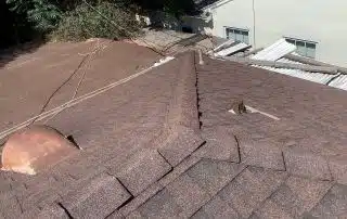 Brown shingle roof with nearby greenery and windows.