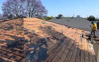 Worker repairing wooden house roof under clear sky.
