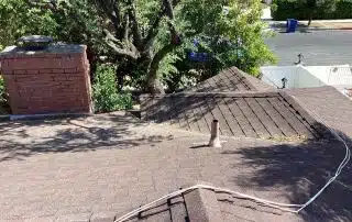 Brown shingle roof with chimney and surrounding trees.