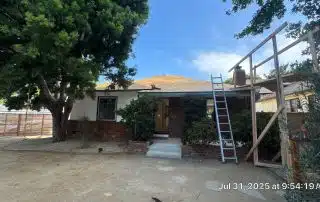 House with ladder and scaffolding under tree canopy.