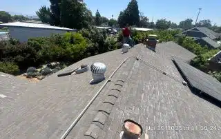 Person inspecting residential roof with vents and chimney.
