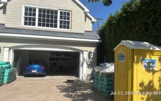 House with open garage and porta potty outside