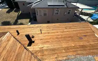 Wooden roof under construction with nearby houses and pool.
