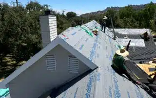 Workers installing roofing underlayment on angled roof.