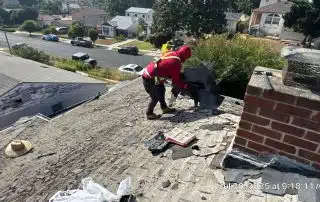 Worker removing roofing shingles on sunny day.