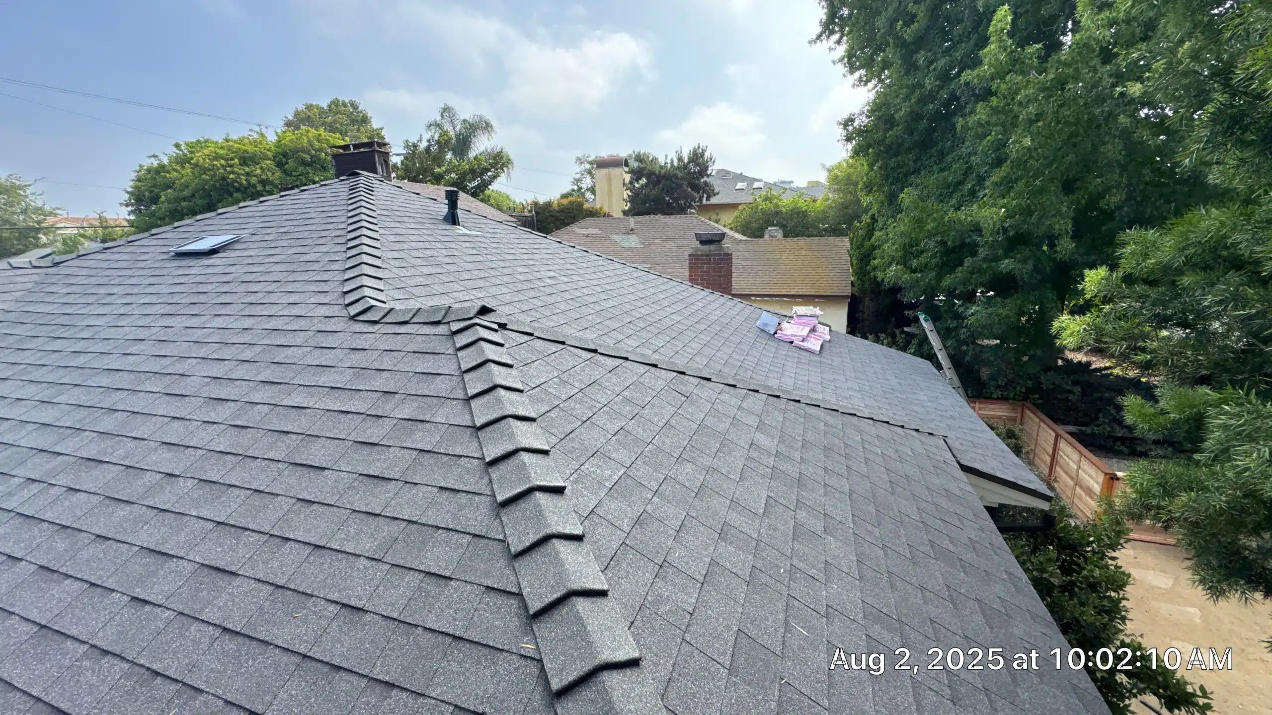 View of a gray shingle roof with surrounding trees.
