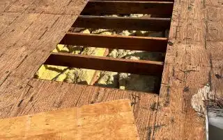 Damaged roof with exposed wooden beams and insulation.