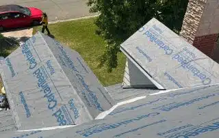 Roofing installation with CertainTeed materials and vehicles nearby.