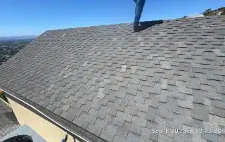 Person standing on shingled roof overlooking cityscape.