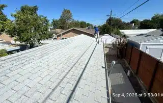 Person on roof inspecting shingles in sunny weather.