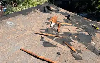 Damaged roof with scattered debris and exposed wood.