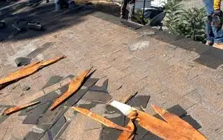 Workers repairing damaged roof with shingles removed.