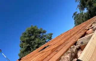 Wooden roof construction under blue sky with trees.