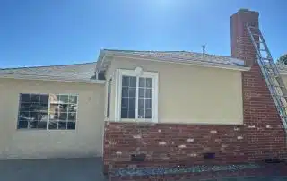 Sunlit house exterior with brick chimney and ladder