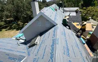 Workers installing roof shingles on residential rooftop.