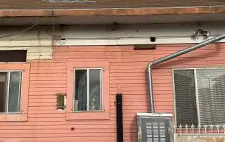 Weathered pink house facade with windows and a chair.