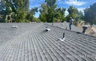 Worker inspecting residential rooftop under clear sky.