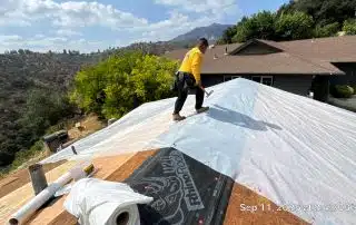 8-Sep 11 2025 02_42pm-m8NS Worker installing roof tarp on house roof.