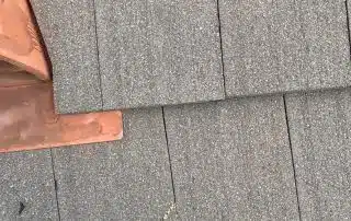 Person standing on shingled roof near chimney flashing.