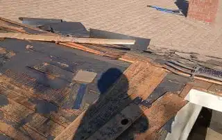 Damaged roof shingles under repair on sunny day.