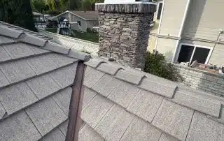 Gray shingled roof with chimney and trees backdrop.