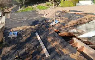 Damaged roof under repair with exposed wood beams.