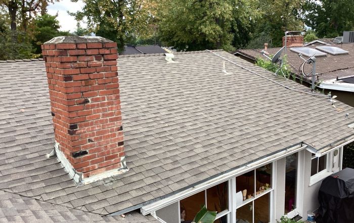 Shingled house roof with brick chimney and gutters