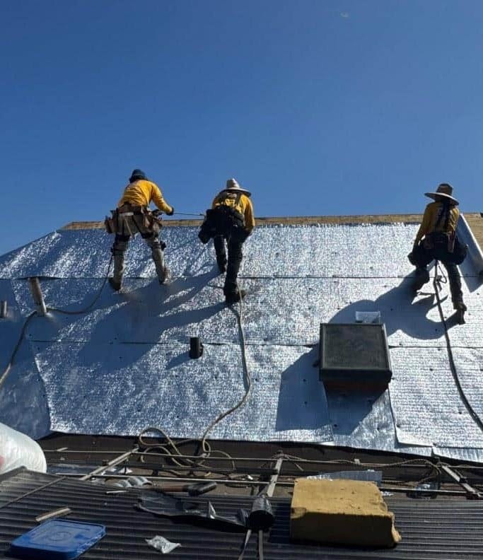 emergency-roof-repair-crew-underlayment-los-angeles Roof Repair and Construction Inc. crew installing radiant barrier underlayment across a stripped roof deck