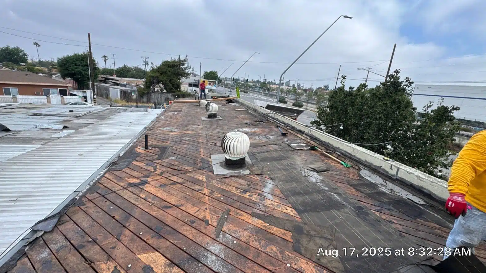 Stripped flat roof deck with worn wood planking and turbine vents exposed during commercial tear-off in Los Angeles County