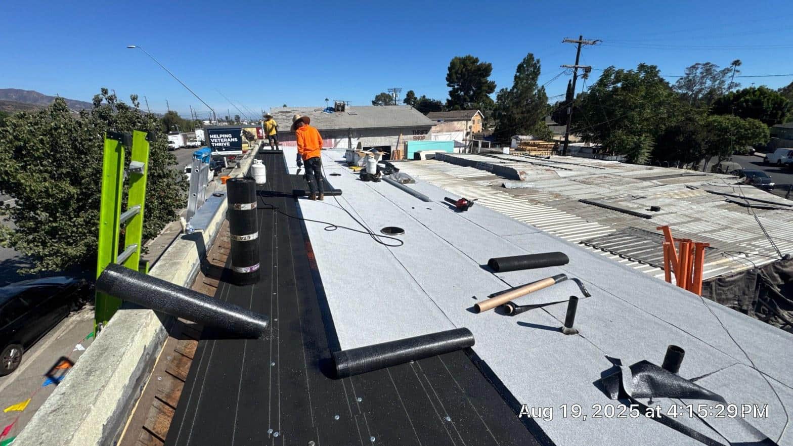 Crew torch-applying modified bitumen cap sheet on commercial flat roof with base sheet already installed, August 2025