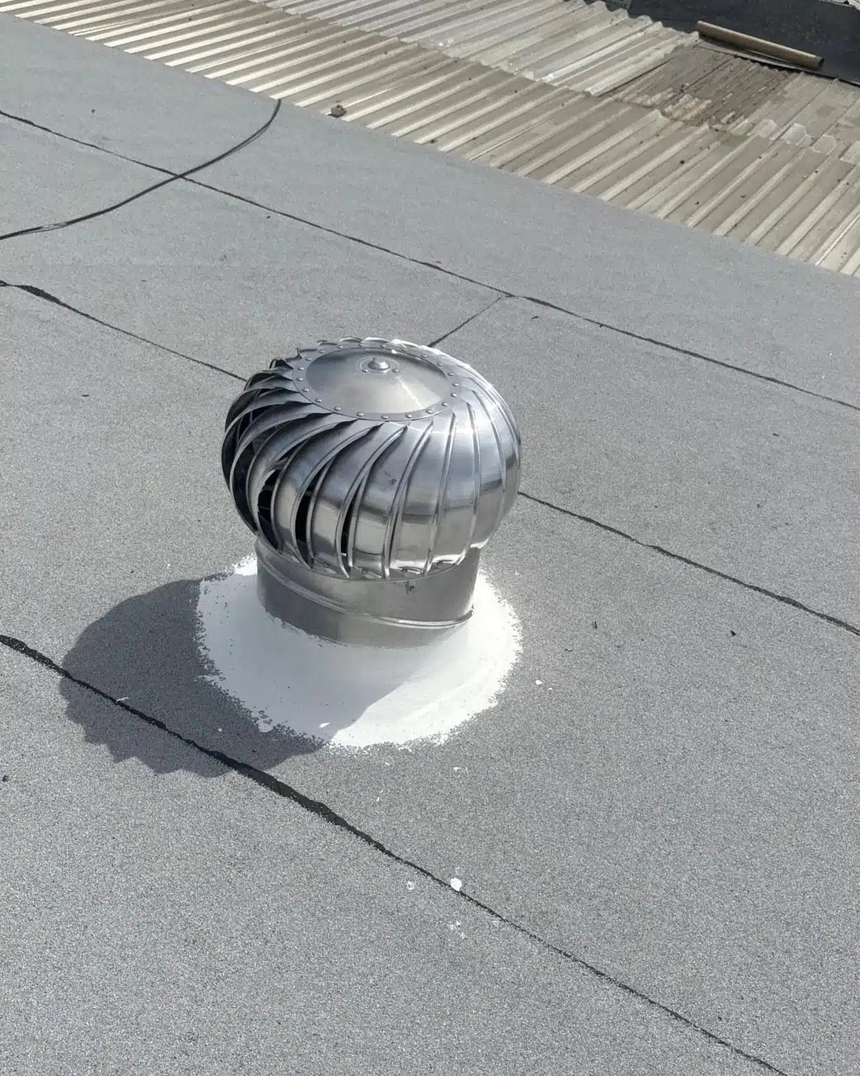 Stainless steel turbine vent with elastomeric sealant collar sealed into torch-down modified bitumen roofing membrane