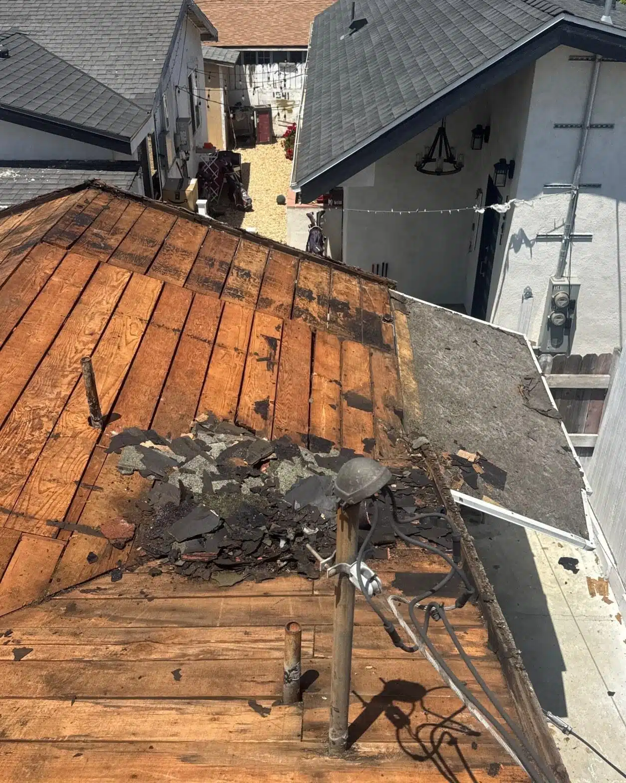 Bare wood roof decking exposed after shingle tear-off, showing debris and moisture-damaged boards on LA County home
