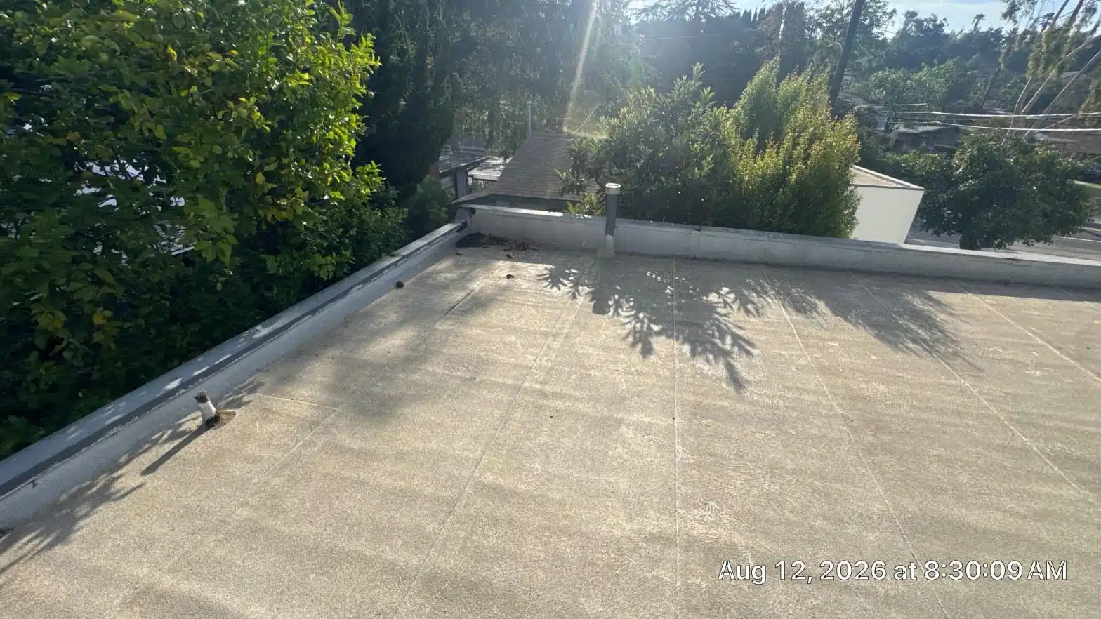 Aged flat roof membrane with oxidation, seam lines, and parapet walls on Los Angeles County residential building