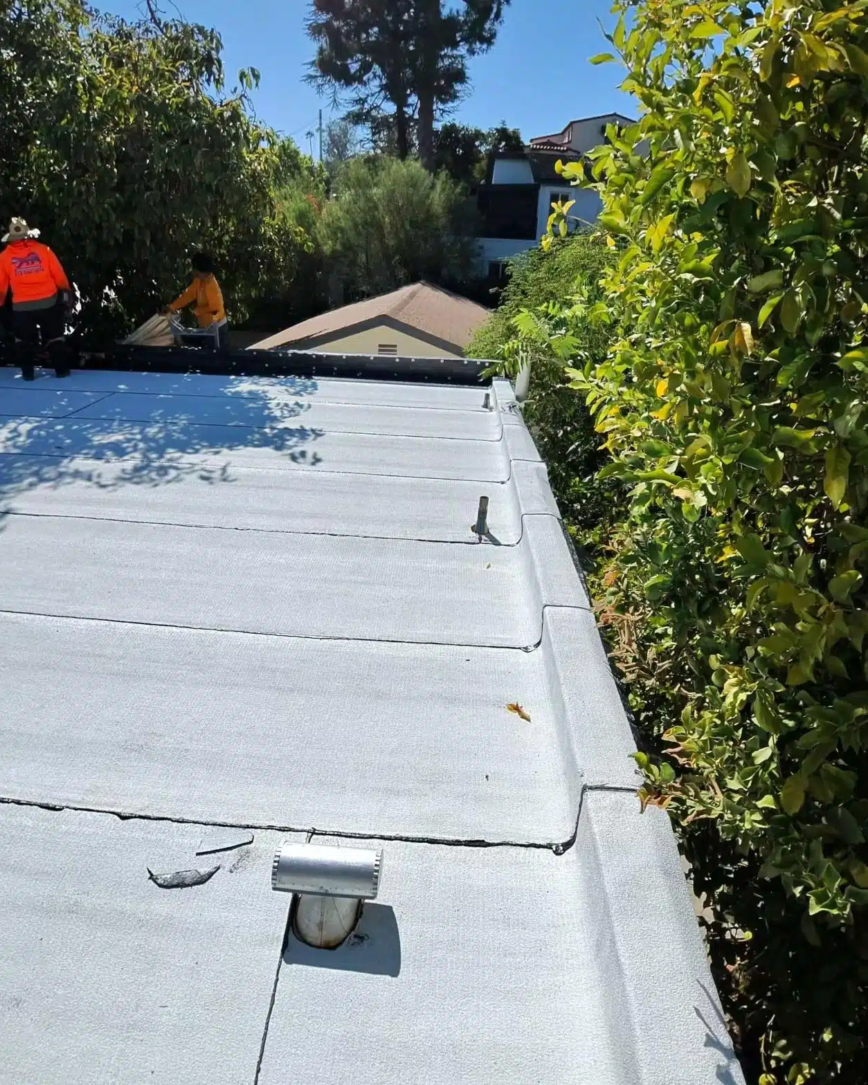 Crew installing white reflective torch-down membrane on residential flat roof in Los Angeles County